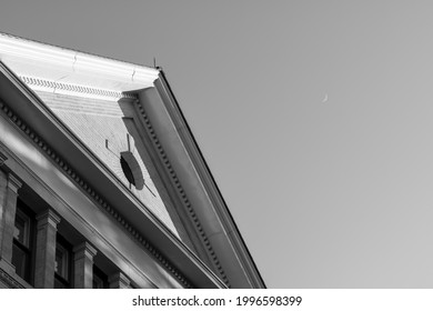 Black And White Of Peaked Gabled Roof With Oculus Window On Exterior Facade. Sliver Moon In Sky. Room For Text. 