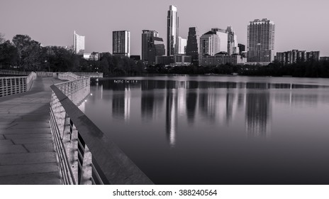 black and white pedestrian riverside bridge on town lake next to the mirror image water of colorado river the austin texas skyline cityscape 