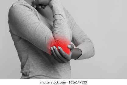 Black and white photo of african woman holding her elbow, pain zone highlighted with red, joint problems