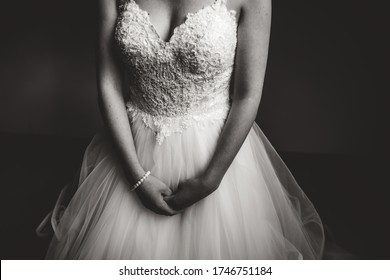 Black and white photo of bride in white wedding dress holding her hands in front of body. Focused on hands. Wedding day concept.