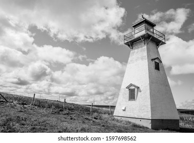 A Black And White Photo Of A Classic, 19th Century Wooden Lighthouse Under Large Storm Clouds.