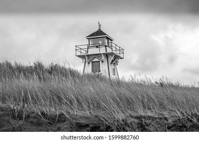 A black and white photo of a classic, 19th century wooden lighthouse above grassy beach sand dunes under a stormy sky. - Powered by Shutterstock