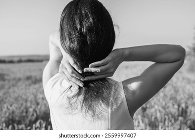 black and white photo Close-up of a woman's hands adjusting her long dark hair with a purple wildflower, set against a golden wheat field at sunset. Natural beauty, summer tranquility - Powered by Shutterstock