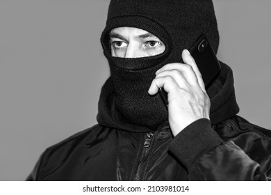 Black And White Photo Criminal In A Black Balaclava And A Hoodie In The Dark. The Concept Of Crime Growth, Robbery And Fraud, Unemployment And Malice.