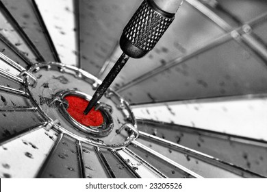 Black And White Photo Of Dart Board With Red Bulls Eye And Dart In The Middle.