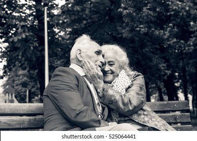 Black And White Photo. Elderly Family Couple Talking On A Bench In A City Park. Happy Seniors Dating