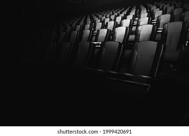 black and white photo, empty cinema. The red and black armchairs in the cinema hall are illuminated by a beam of light, a low key. Selective focus. Quarantine, restrictive tape on chairs 