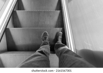 Black and white photo of feet in trainers standing on a moving escalator on the London Underground. London - 28th May 2022