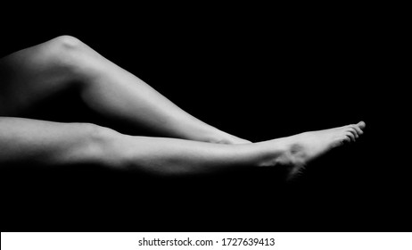 black and white photo of female legs lying on a black void and pulling toes, side view isolated on black background