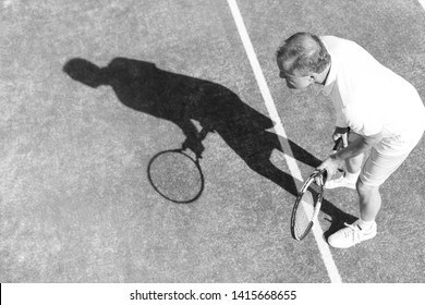 Black And White Photo Of Full Length Of Senior Man Playing Tennis On Red Court During Summer Weekend