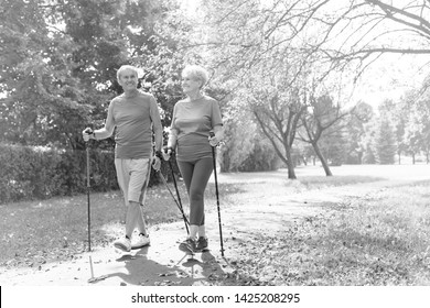 Black And White Photo Of Happy Senior Couple With Hiking Poles Walking In Park