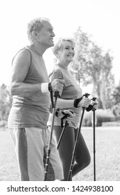 Black And White Photo Of Healthy Senior Couple With Hiking Poles Walking In Park