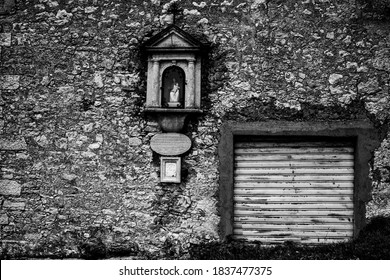 black and white photo of a house facade with closed vintage shutter and capital with Madonna and child