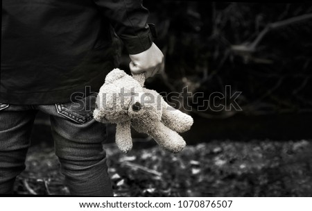 Black and white photo of Kid holding teddy waking alone in the forest, Rear view of a Boy standing alone holding his ted, Spoiled child, lost children or homeless kid concept
