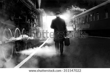 Black and white photo of man in vintage clothes walking on old railway station