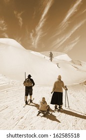 Black And White Photo, Man And Woman With Old Wooden Skis And Child On Sled On Snowy Mountain 