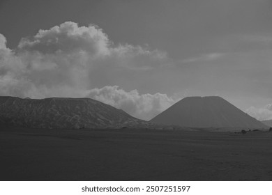 A black and white photo of a mountain range with a volcano in the background. Scene is serene and peaceful, with the mountains and volcano creating a sense of awe and wonder - Powered by Shutterstock