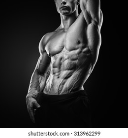 Black and white photo of Muscular and fit young fitness model posing over black background. Strong bodybuilder with six pack, perfect abs, shoulders, biceps, triceps and chest.