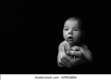 Black And White Photo Of Newborn Baby On An Isolated Black Background On His Father's Hands