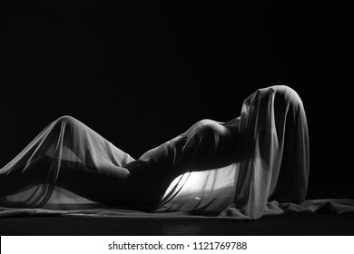 Black and White photo in Nude Artistic sensual sexy look of beautiful figure girl under hiding in light thin fabric, to show silhouette of woman body lying on floor, up waist chest female in shadow