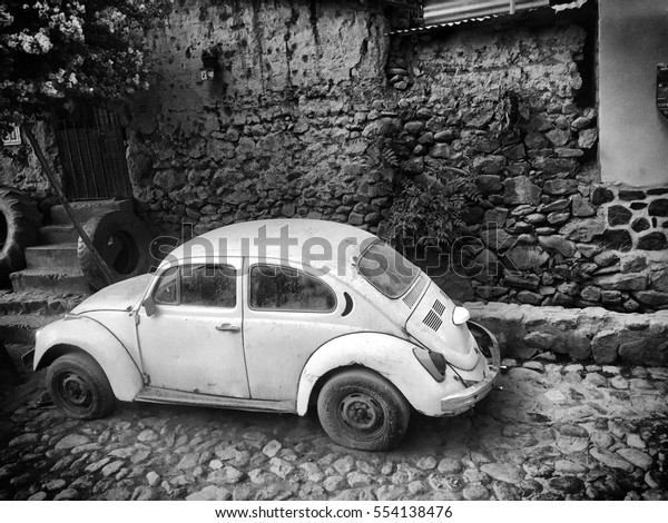 Black and white photo of an old VW Bug on a\
street in Ollantaytambo on May 11,\
2016