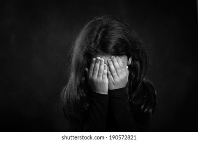 Black and white photo. Portrait of a crying girl. She is covering her face.