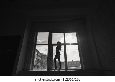 Black and white photo of a pregnant young woman near a window. Silhouette of a pregnant woman.