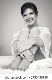 Black And White Photo Of A Pretty Bride Sitting On The Bed Holding Her Arms Around Her Legs.