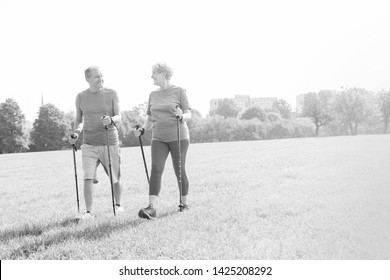 Black And White Photo Of Senior Couple With Hiking Poles Walking On Grassy Field