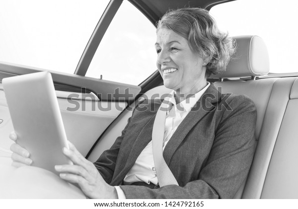 Black and White photo of Smiling businesswoman using\
digital tablet in car 