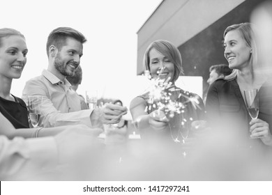 Black and White photo of Smiling colleagues holding sparklers during party on rooftop - Powered by Shutterstock