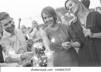 Black and White photo of Smiling colleagues with sparklers during party on rooftop - Powered by Shutterstock