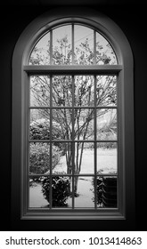 Black And White Photo Of Snow Falling Outside Framed By A Beautiful Window.