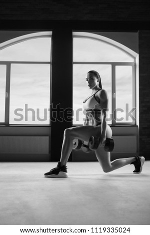 Black and white photo of strong woman doing fitness exercises with dumbbells. Looking healthy, strong, fit, feeling good. Going to gym. Having athletic muscles and stunning figure, body.