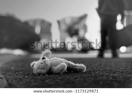 Black and white photo of Teddy bear laying  on the street with blurry background of school kid carrying school bag,Toy bear was left lying on the street,missing children or kidnap school kids concept