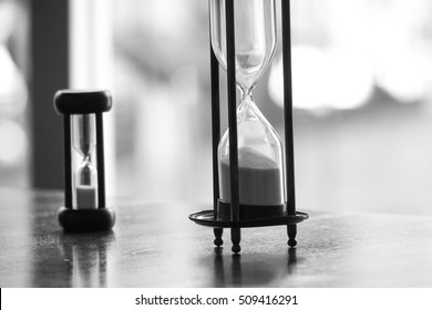 Black And White Photo Of Two Difference Size Of Vintage Sandglass Or Hourglass Or Egg Timer On The Table Showing The End Of Time