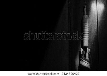 black and white photo of an umbrella illuminated by light penetrating the roof of a house