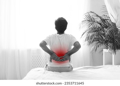 Black and white photo of unrecognizable man in pajamas touching lower back while sitting on bed at home, young male suffering from acute backache in the morning, uncomfortable sleeping concept - Powered by Shutterstock