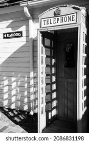  Black And White Photo Of A Vintage Telephone Booth Against A White Building.