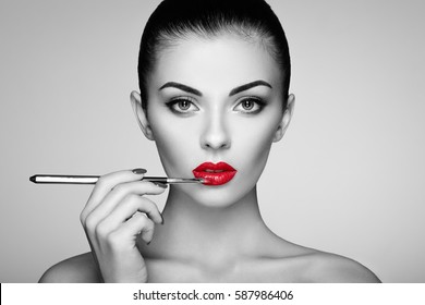 Black and white photo of woman painting lipstick. Beautiful woman face. Makeup detail. Beauty girl with perfect skin. Red lips and nails manicure