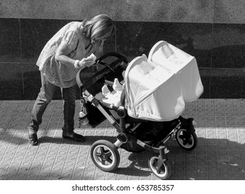 Black And White Photo Of Woman Pushing Double Stroller With Hood Up