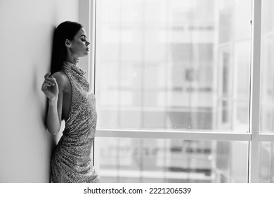 Black and white photo of a woman in a stylish sequined party dress posing near a window bw