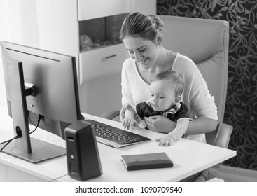 Black And White Photo Of Young Owman Sitting With Her Baby Son Behind Computer Desk At Office