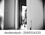 A black and white photograph captures a person walking through a doorway