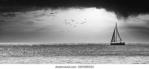 Black and white photograph of a sailboat sailing in a dramatic sunset - Powered by Shutterstock