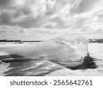 Black and white photograph of a small iceberg stuck between ice on a river 