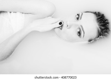 Black And White Photography Of Beautiful Tender Young Woman Touching Her Lips With Finger Lying In The Water On Light Background. Closeup Portrait