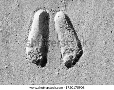 Black and white photography of human feet prints in the sand.