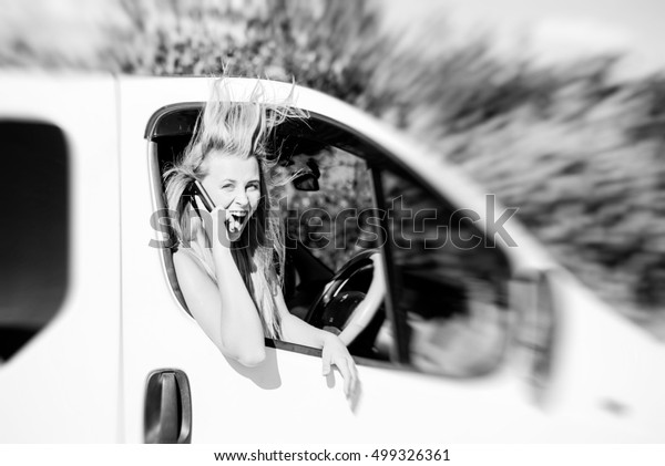 Black and white photography of joyful excited\
woman driving car van talking on mobile phone on sunny summer\
countryside background\
outdoors