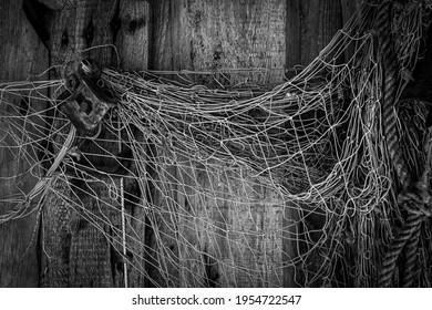 Black And White Photography Of Old Weathered Fishers Nets, Ropes And Rusted Metal Screw Hanging On Wooden Hatch Wall